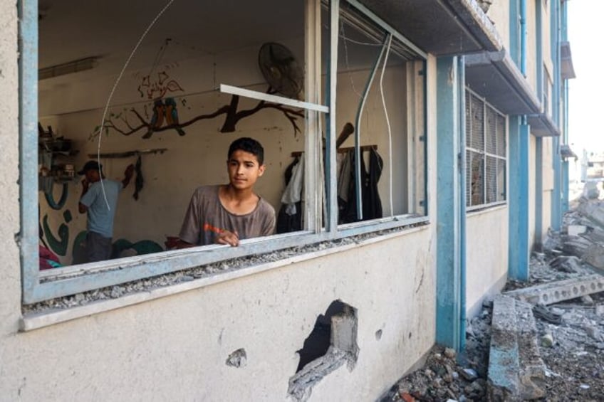 A Palestinian boy stands by a shattered window at a UN school sheltering displaced people