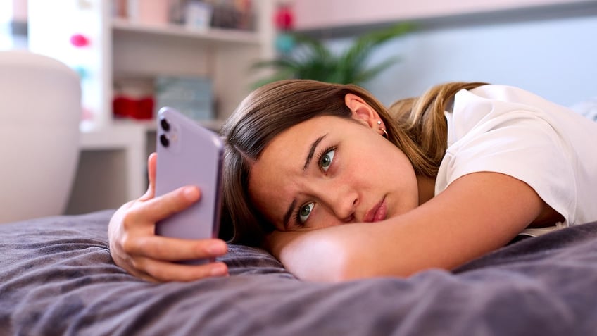 Teenage Girl Lying On Bed At Home Looking At Mobile Phone