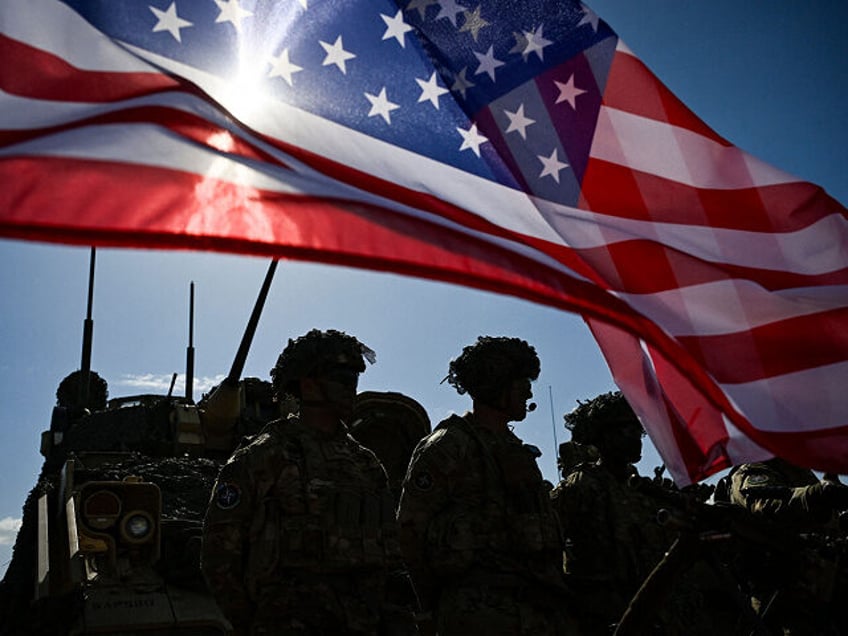 US Army soldiers stand in formation next to a US flag and a US Army armoured vehicle as th