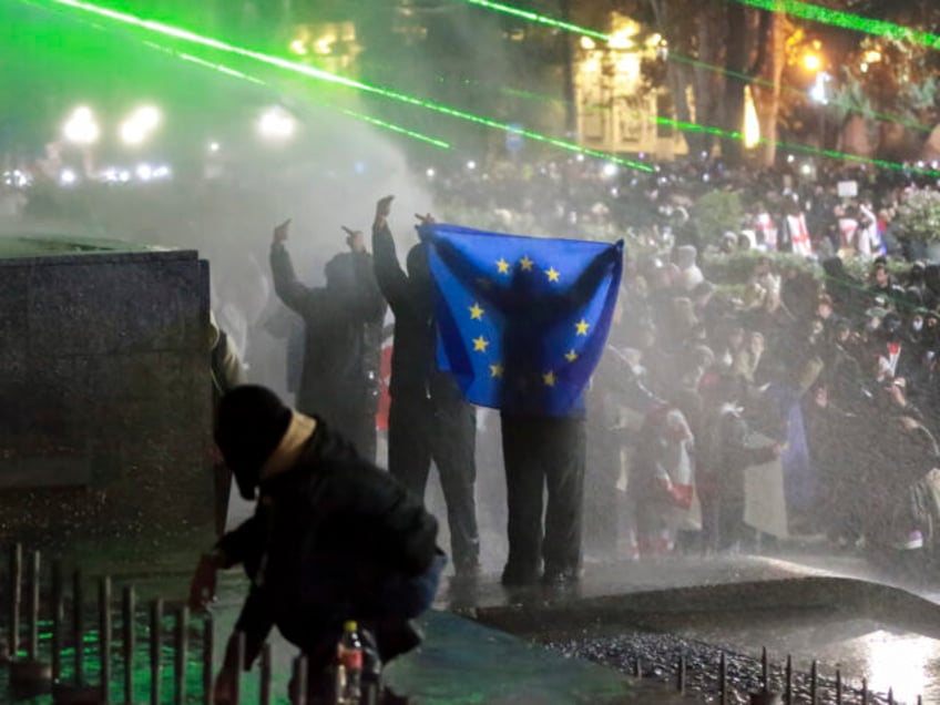 Demonstrators with an EU flag stand atop of a tomb under running water from a water cannon