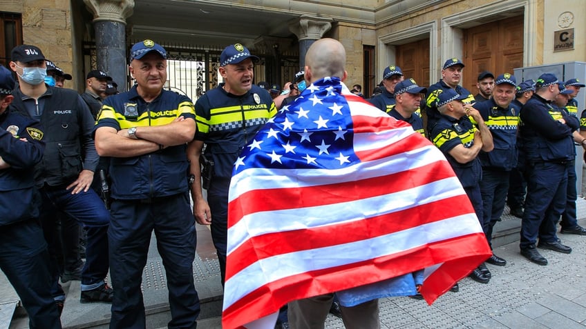 A demonstrator draped in an American flag stands in front of police during an opposition protest against the foreign influence bill at the Parliamentary building in Tbilisi, Georgia.