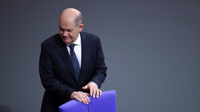 German Chancellor Olaf Scholz stands behind chair