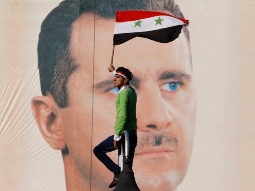 FILE - A pro-Syrian regime protester waves a Syrian flag as he stands in front of portrait