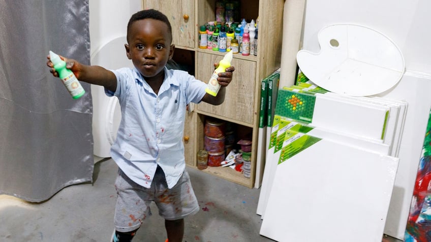 Ace-Liam Nana Sam Ankrah, who will turn two in July, shows off his green and yellow paint tubes at his mother's art gallery in Accra, Ghana.
