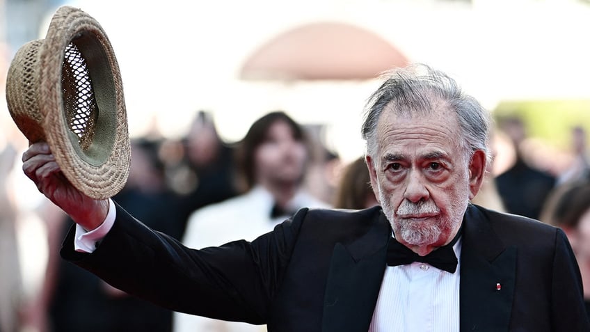 Francis Ford Coppola holding out his hat on the red carpet