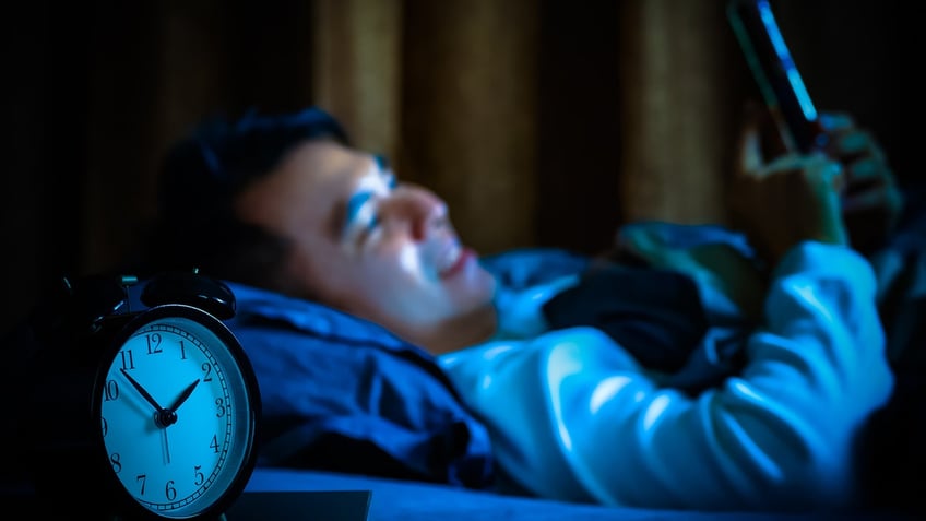 man playing on smartphone in bed at night