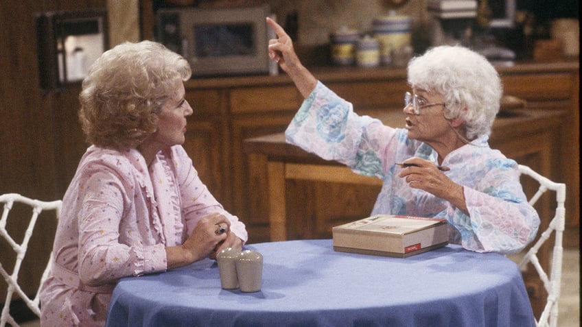 Betty White in pink looks at Estelle Getty in a patterned outfit on the set of "Golden Girls" as Rose and Sophia