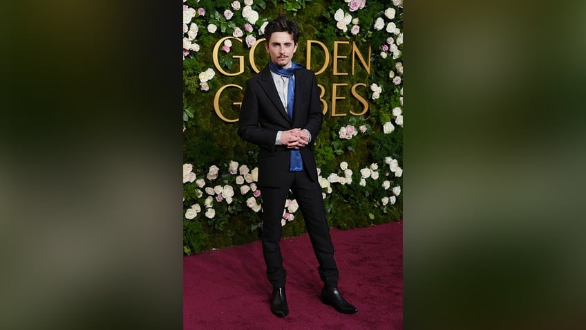 Timothee Chalamet looked dapper as her walked the red carpet in a black suit and a blue scarf at the 2025 Golden Globe Awards.