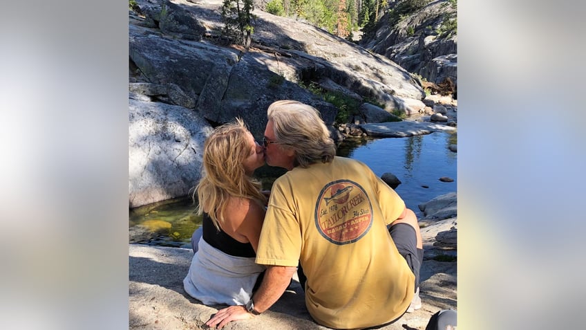 Goldie Hawn and Kurt Russell give each other a kiss on top of a rock 