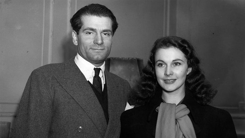 Laurence Olivier in a suit standing next to his smiling wife Vivien Leigh