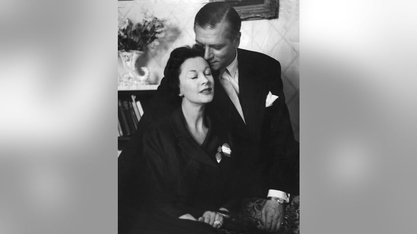 Laurence Olivier in a suit giving Vivien Leigh a kiss on her forehead as she wears all black.