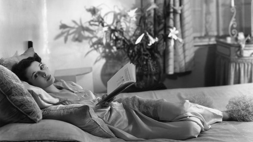 Vivien Leigh laying in bed holding a book.