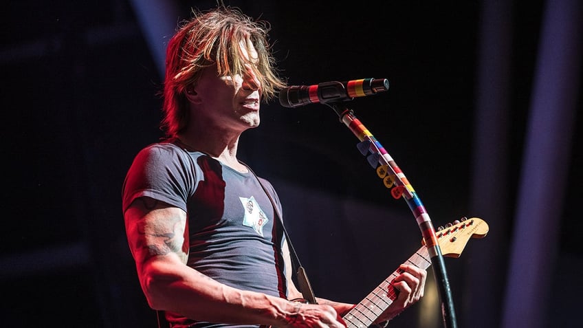 John Rzeznik sings in front of a microphone while holding a guitar.