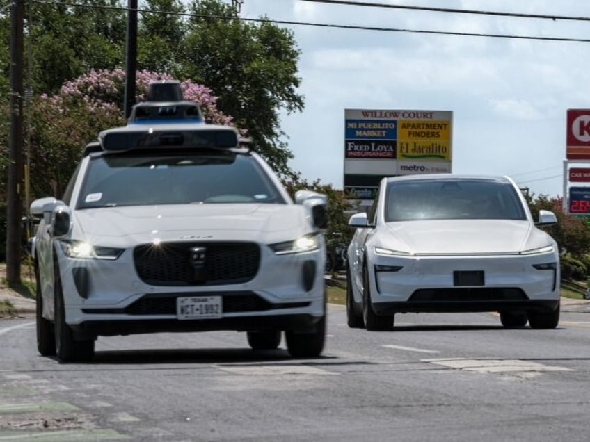 A Waymo robotaxi passes a Tesla on the road