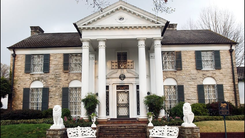 The front of the brown stone home features a black ceiling, white beams, lion statues and two benches at the base of the stairs.