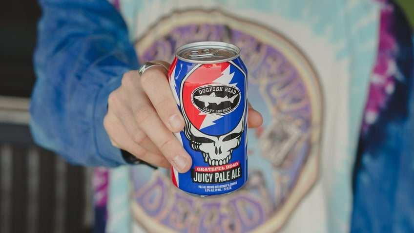 A person wearing a Grateful Dead T-shirt holds a can of Dogfish Head's Grateful Dead Juicy Pale Ale.