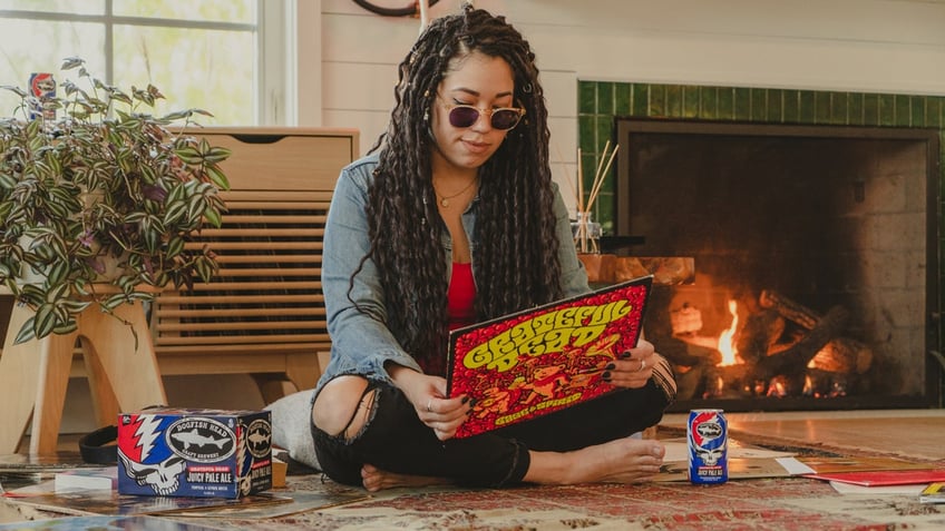 A fan of the Grateful Dead looks at the back of a record while sitting on the floor next to Dogfish Head's Grateful Dead Juicy Pale Ale.