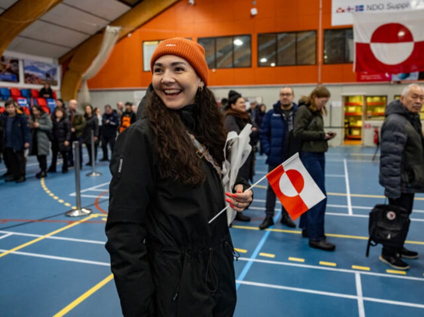 A woman holds a Greenland national flag as she queues to vote at the polling station in Nu