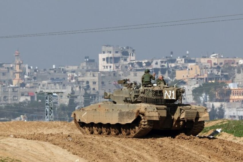 An Israeli tank, photographed from southern Israel, overlooks damaged buildings in the Gaza Strip