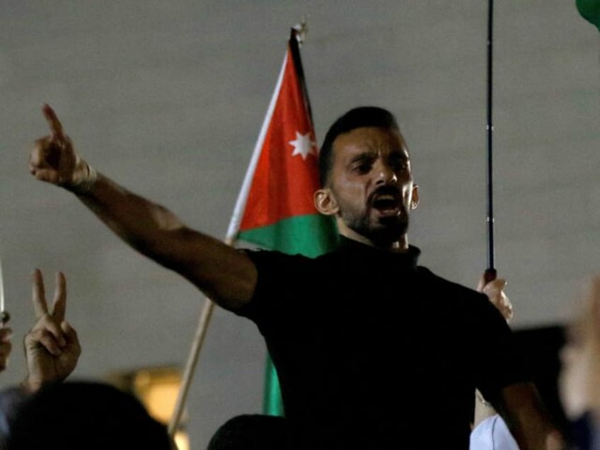 People wave flags as they protest near the Israeli embassy in Amman, to denounce the assas