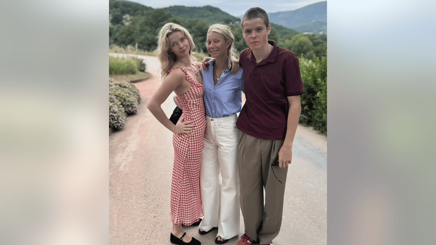 Apple Martin in a red dress poses with mother Gwyneth Paltrow in a blue top and white pants and son Moses in a red shirt and brown pants