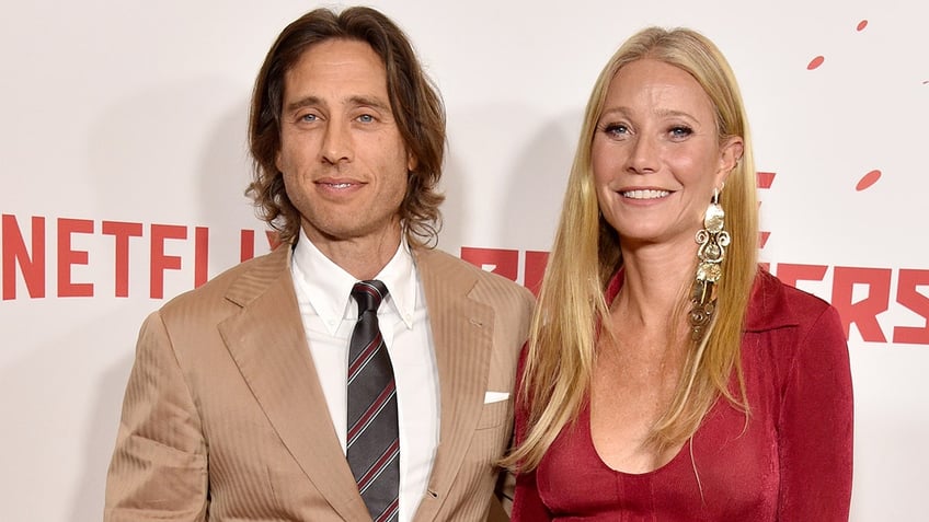 Gwyneth Paltrow in a red dress and Brad Falchuk in a suit hugging on the red carpet