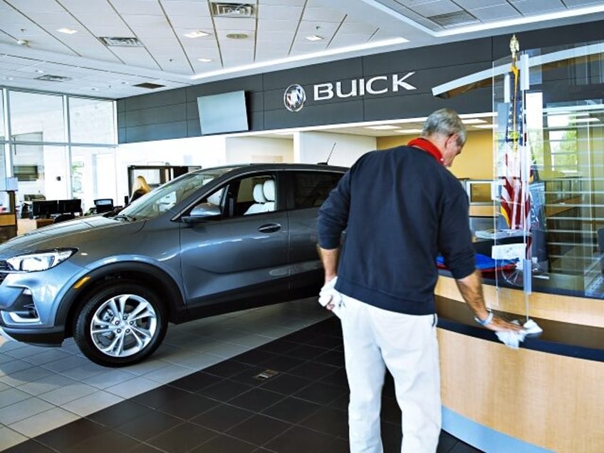 A worker cleans a counter while another worker, wearing a protective mask, sits behind a plastic shield at a General Motors Co. Buick and GMC car dealership in Woodbridge, New Jersey, U.S, on Wednesday, May 20, 2020. Governor Phil Murphy has lifted restrictions on in-person auto sales, provided the businesses …