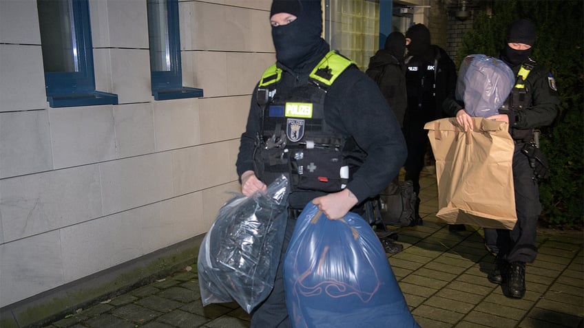 Police officers leave a house with seized evidence