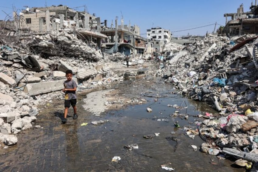 In scorching weather, a boy walks through a puddle of sewage water surrounded by mounds of