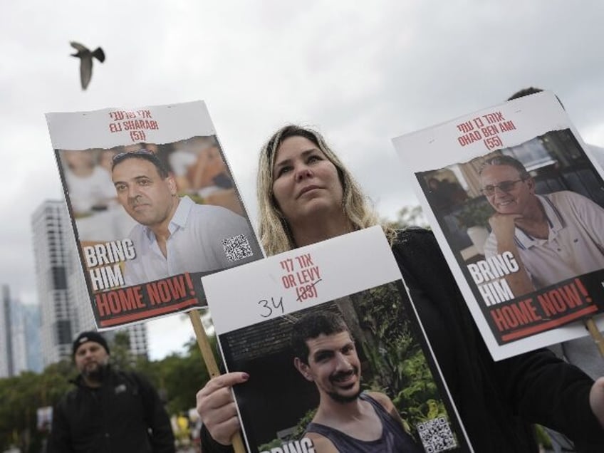 A woman holds posters with photos of Israelis hostages Eli Sharabi, Or Levy and Ohad Ben A