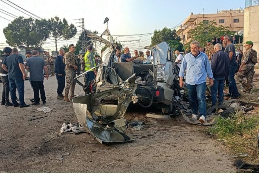 Lebanese soldiers and onlookers gather around the remnants of a car after it was hit by an