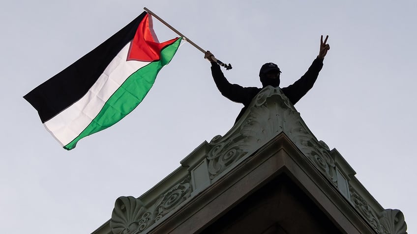 man waves Palestinian flag atop Columbia University building