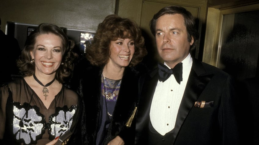 Natalie Wood, Stefanie Powers and Robert Wagner walking in a row together smiling.