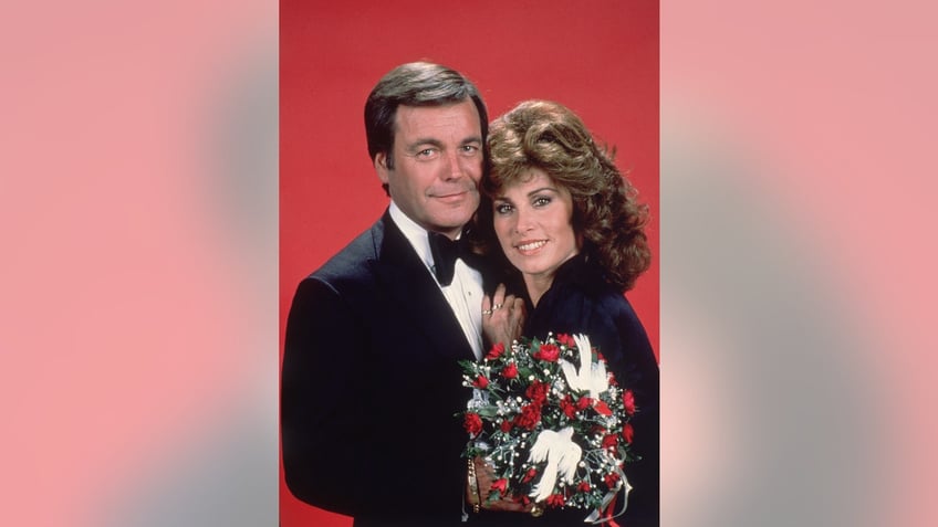 Robert Wagner and Stefanie Powers embracing each other with a bouquet of flowers.