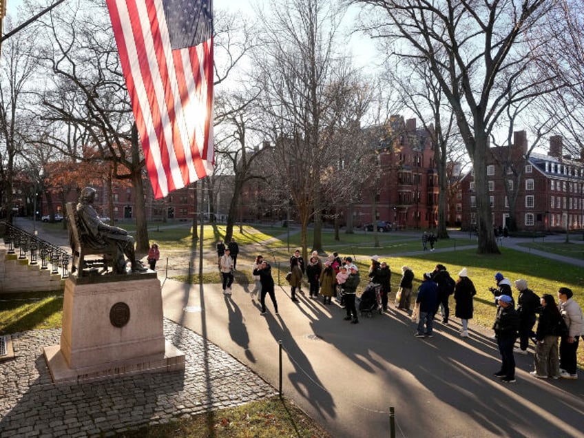People take photos near a John Harvard statue, left, on the Harvard University campus, Jan