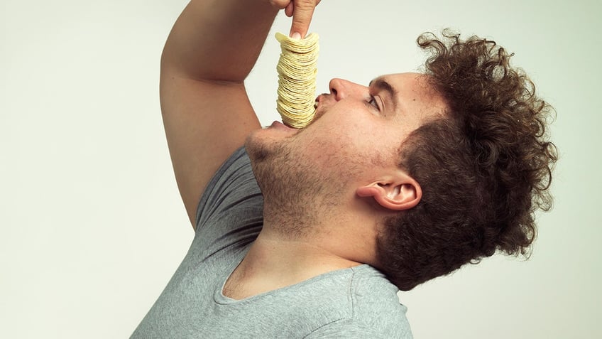 Studio shot of an overweight man shoving a stack of chips down his throat.