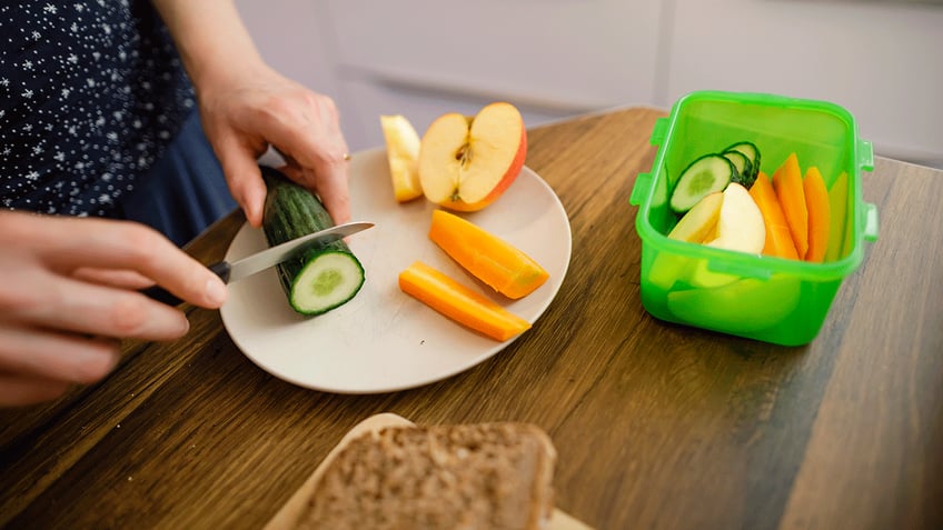Woman cutting fruit and vegetables for kid's lunch