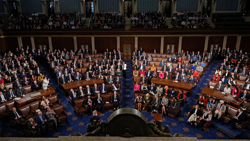 representatives seated in House chamber seen from above looking towards back of chamber