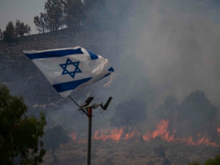 An Israeli flag flutters next to a fire burning in an area near the border with Lebanon, n