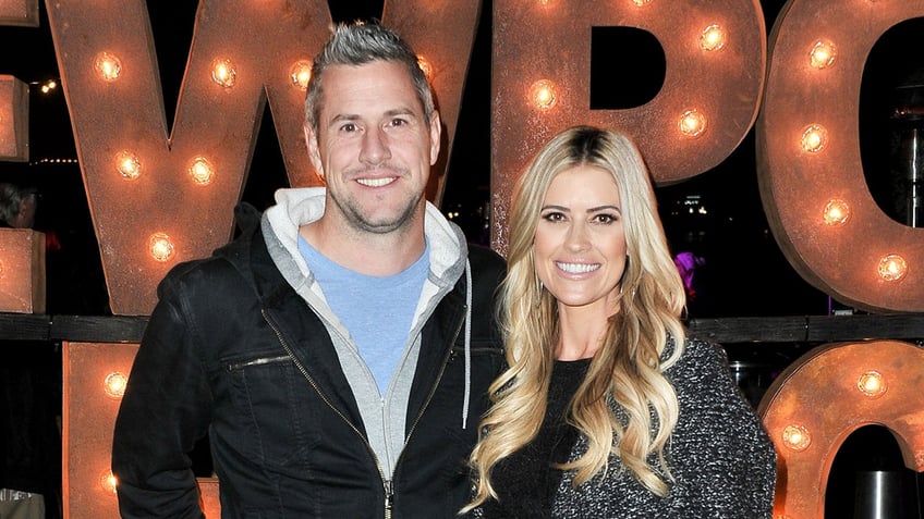 Ant Anstead in a blue shirt and black sweatshirt smliles next to wife Christina in a black and white sweater