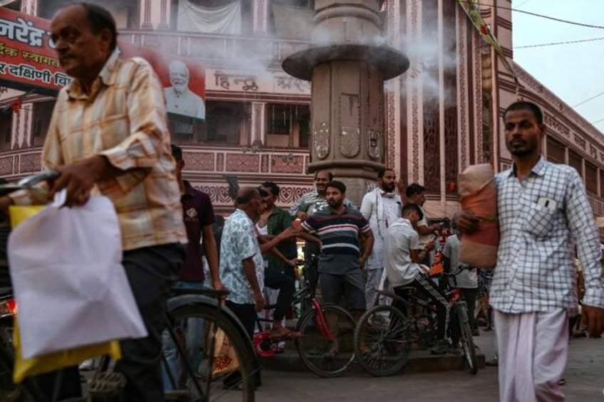 People stand below a water sprinkler installed on a pillar to cool off at a marketplace am