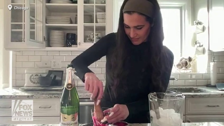 Briana DiTommaso uses a muddler to crush raspberries in a glass while demonstrating the steps for making a holiday cocktail.