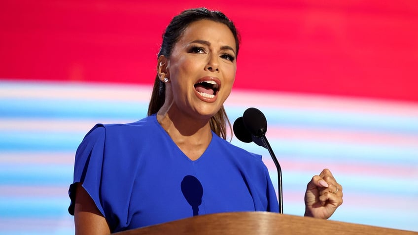 Eva Longoria in a bright blue dress speaks passionately behind the podium at the 2024 DNC