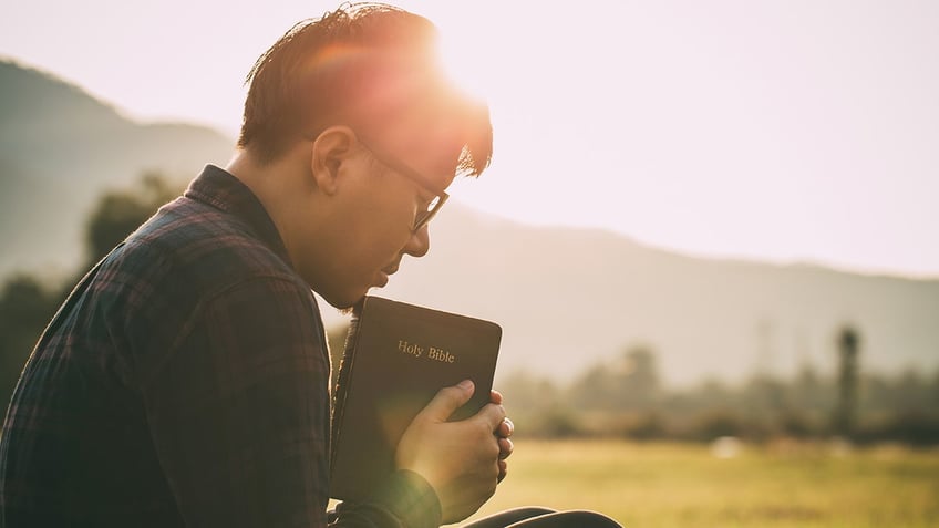 man praying while holding bible