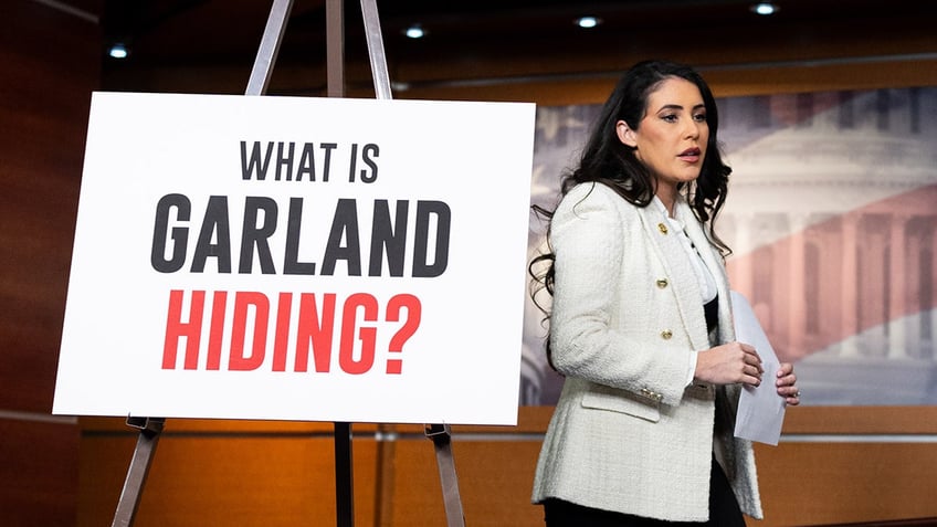 Anna Paulina Luna walks in front of What is Garland hiding poster