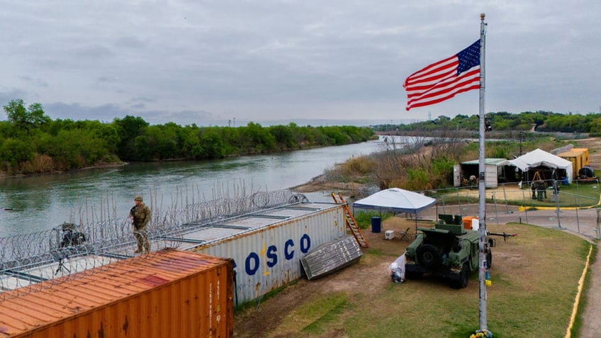 Eagle Pass, Texas river bank seen in aerial view with Guardsmen atop shipping containers