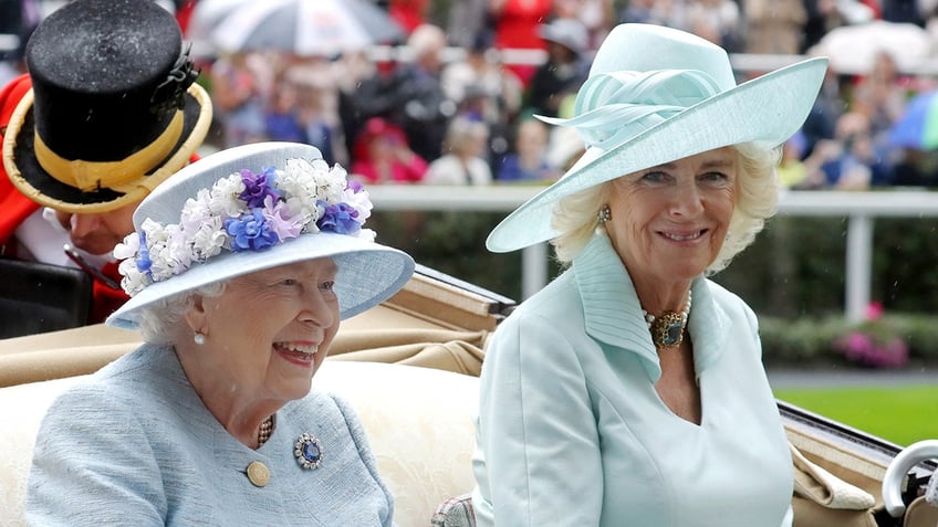 Camilla in a sea green outfit and matching hat sitting in a carriage next to Queen Elizabeth II