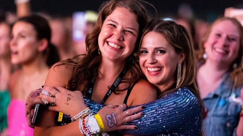 Two fans smile at the Eras Tour in Atlanta, showing off the 13's on their hands