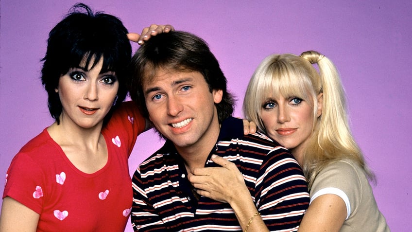 A close-up of Joyce DeWitt, John Ritter and Suzanne Somers against a lilac backdrop