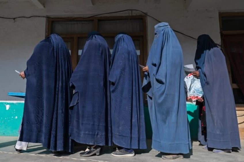 Burqa-clad women stand in a queue as they wait to receive food being distributed in Baraki